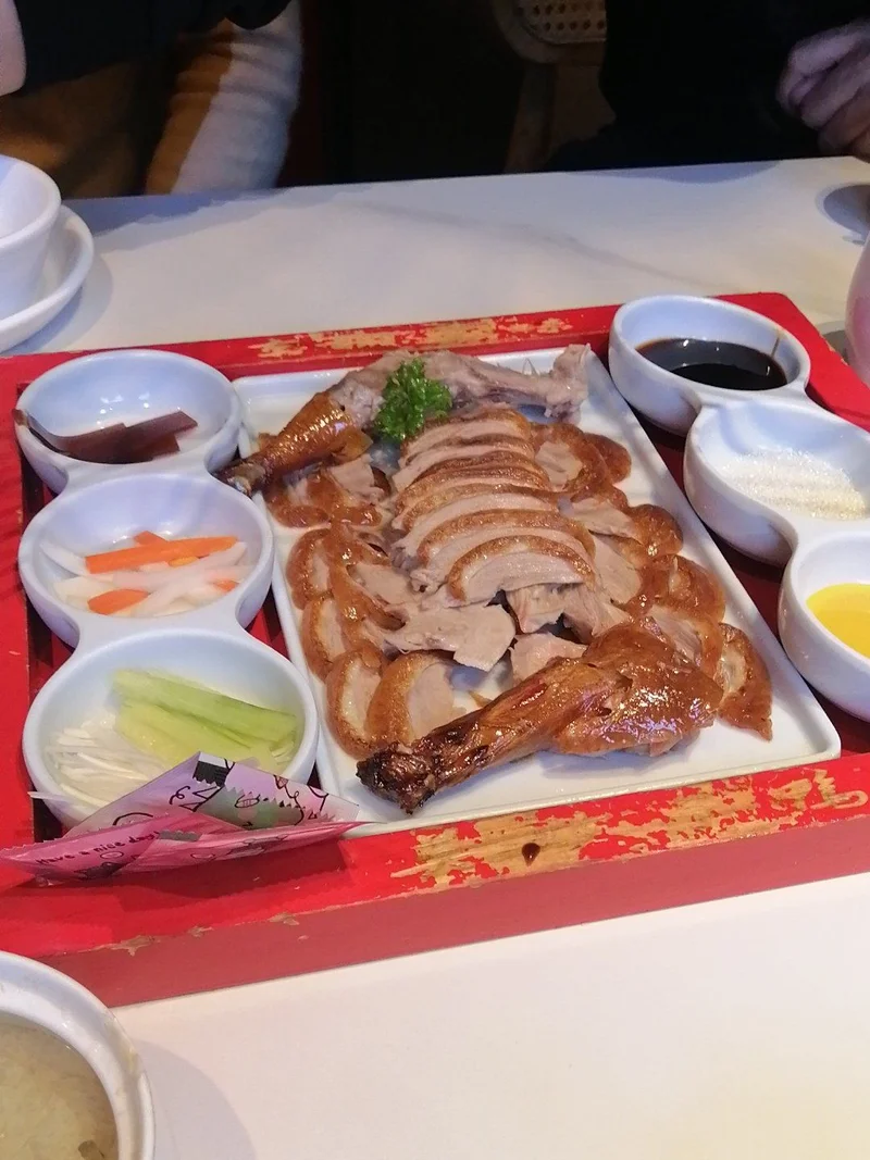 A complete Peking Duck set with sliced duck, pancakes, scallions, cucumber, and sauces.