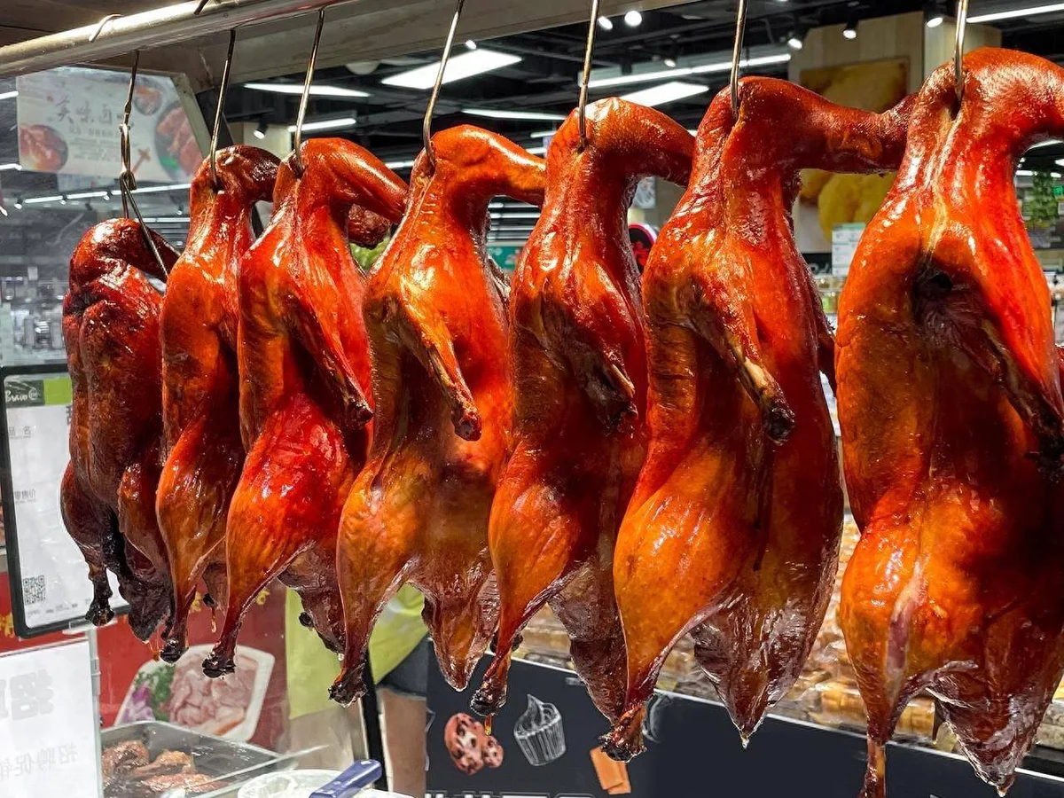 Rows of roasted Peking Ducks hanging to cool with bright golden-red skin.