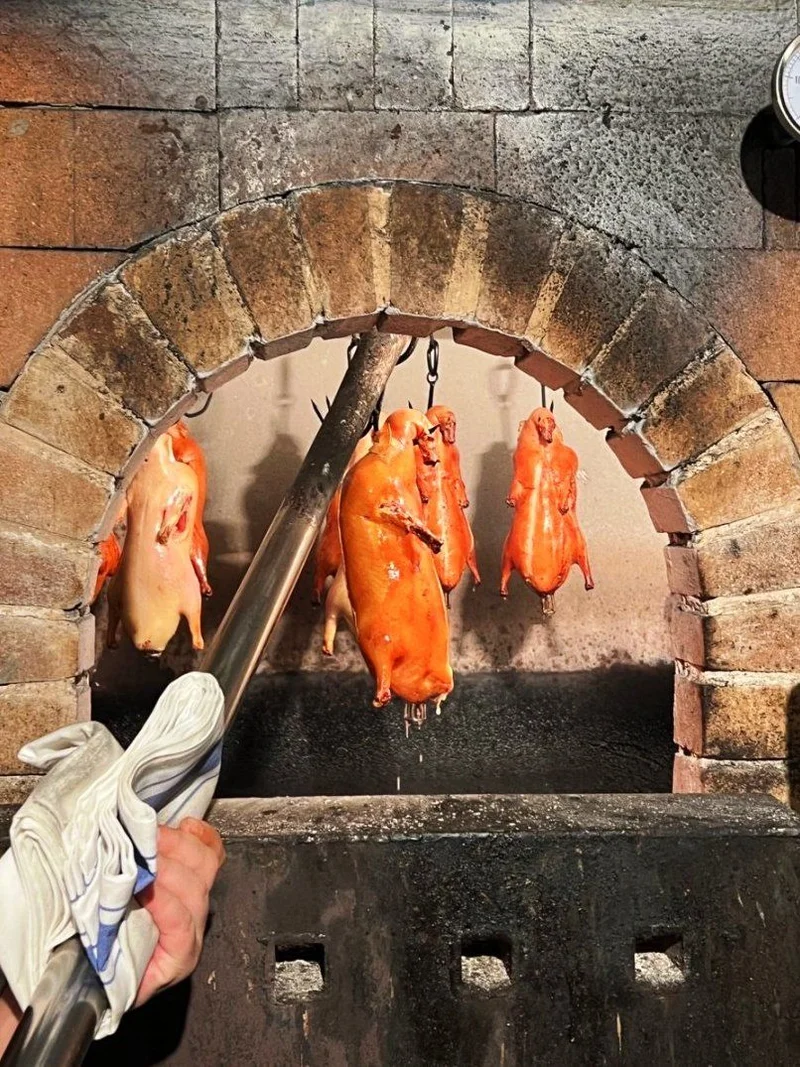 Peking Ducks hanging in a brick oven over fruitwood fire during traditional roasting.