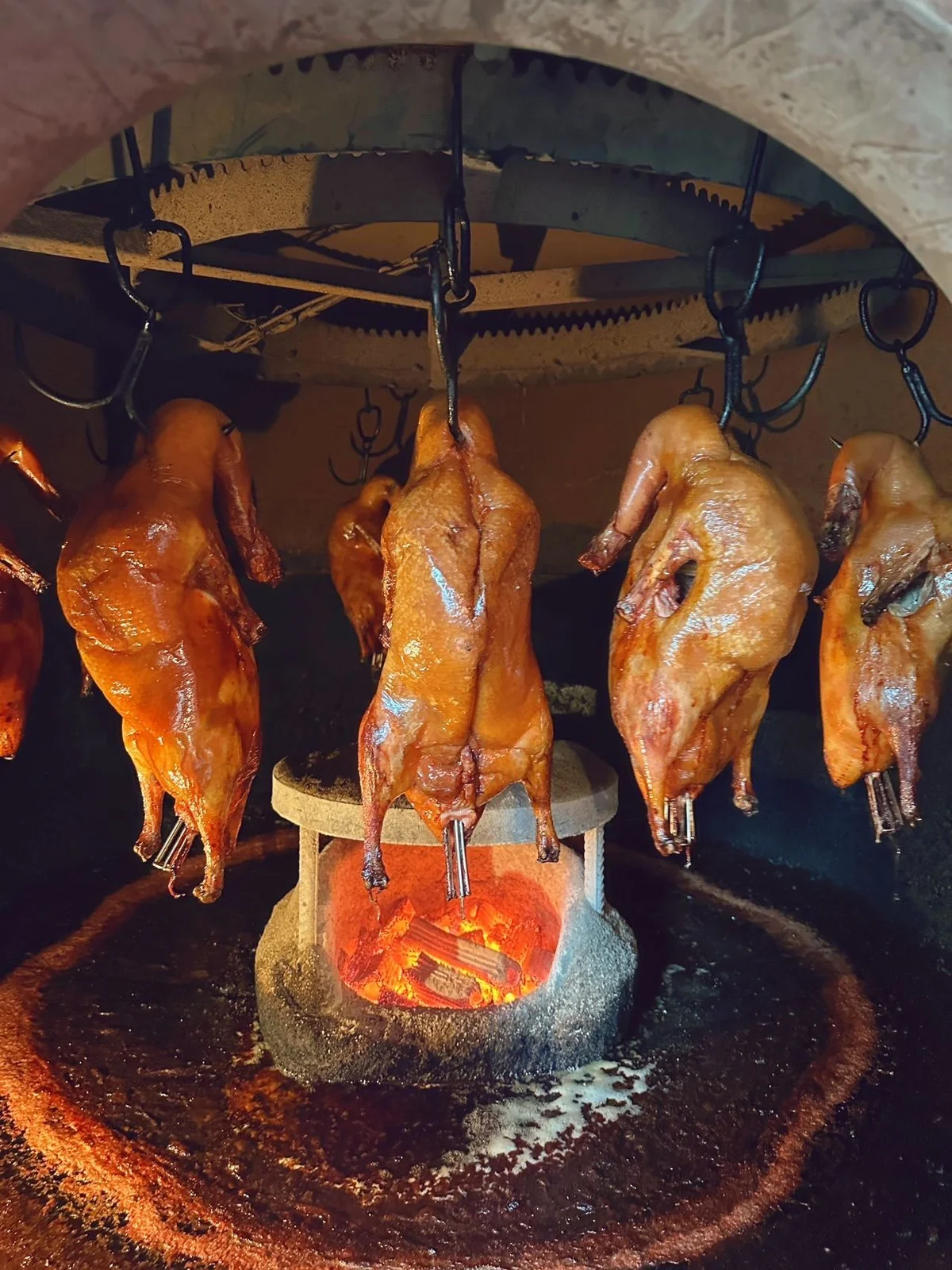 Peking Ducks roasting over a central fruitwood fire, demonstrating the hanging method used in Beijing.