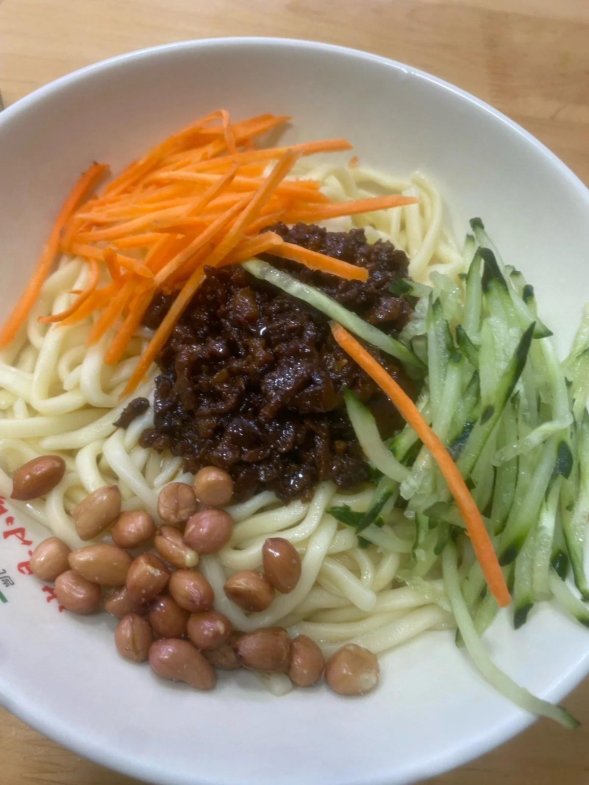 Beijing Zhajiang Noodles topped with carrot, cucumber, peanuts, and fried soybean paste.