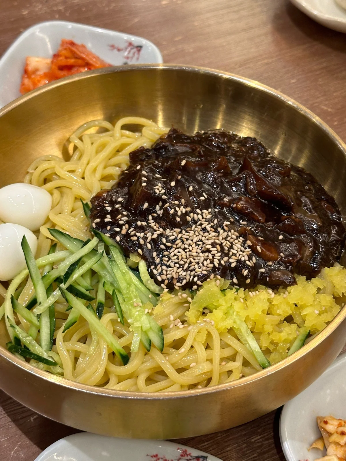 Korean Jajangmyeon served with black chunjang sauce, cucumber strips, pickled radish, quail eggs, and sesame seeds.