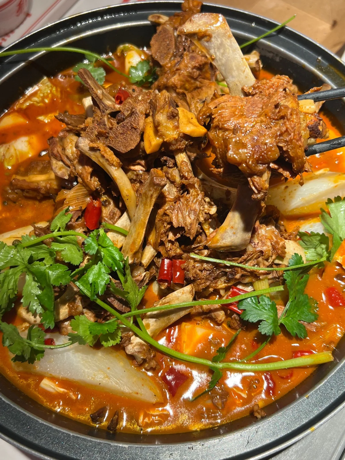 Spicy red-broth lamb spine hotpot featuring bone-in lamb pieces, chili oil, and cilantro, capturing the hearty and warming essence of Beijing’s winter cuisine.