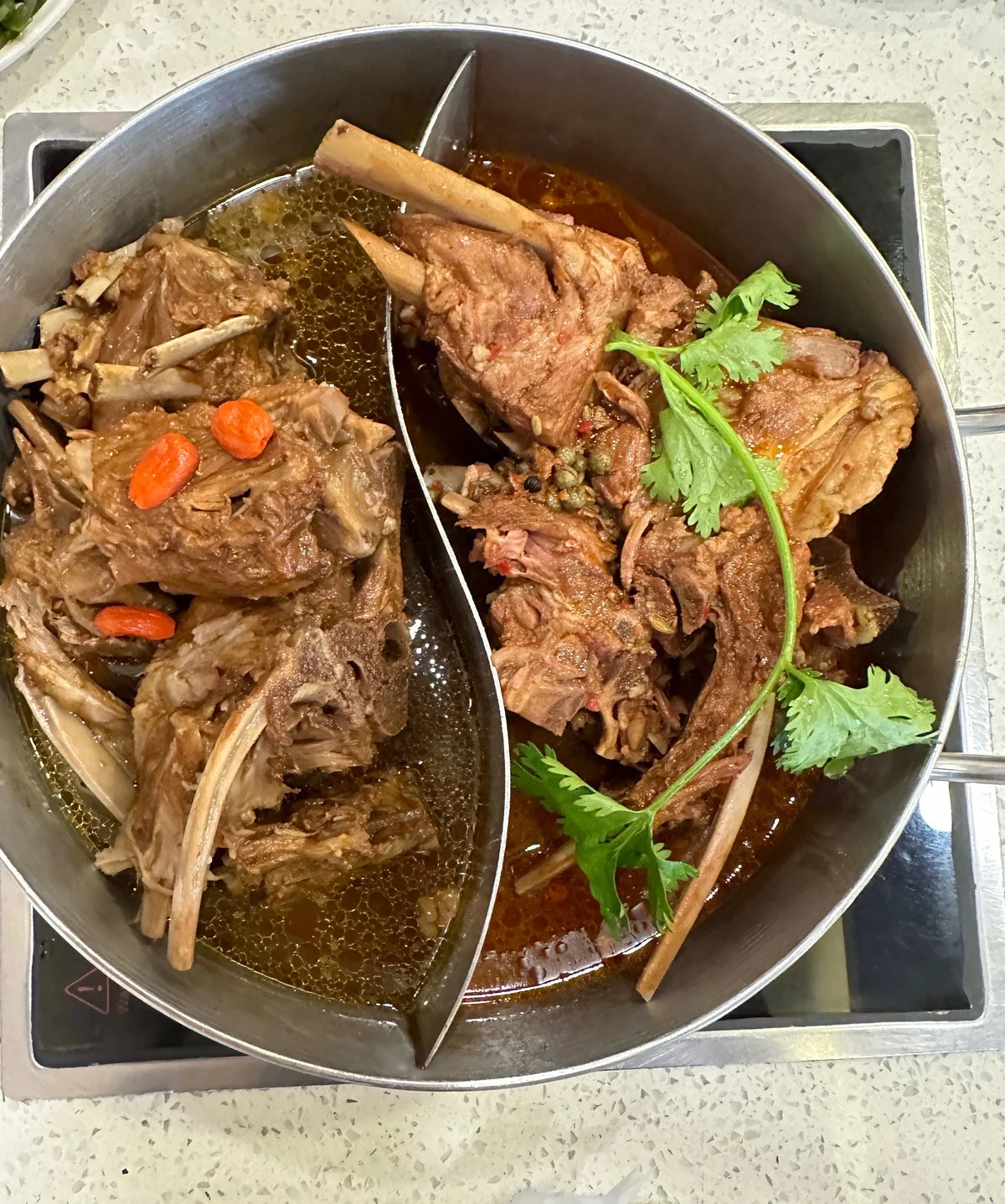 Yin-yang style lamb spine hotpot with clear broth and spicy broth, showcasing large meaty lamb spines simmered with goji berries, herbs, and warming spices.