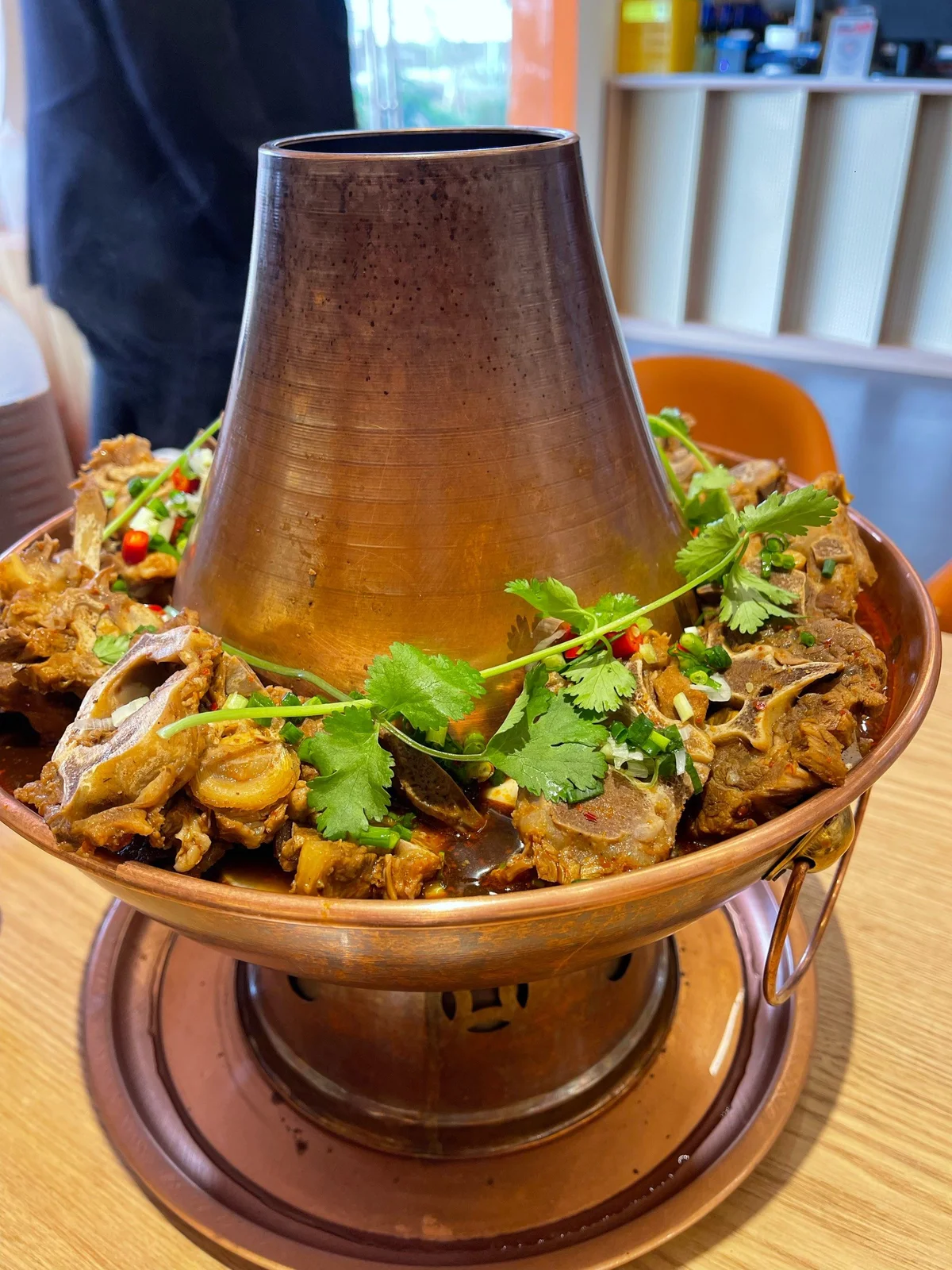 Traditional Beijing lamb spine hotpot served in a copper pot, featuring tender lamb bones simmered in a rich, spiced broth and garnished with fresh cilantro and chilies.