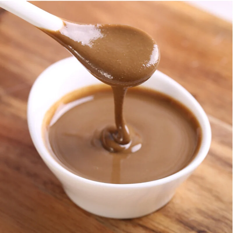 Creamy sesame paste being poured into a small bowl, commonly used as a rich dipping sauce for Yang Xiezi hotpot.