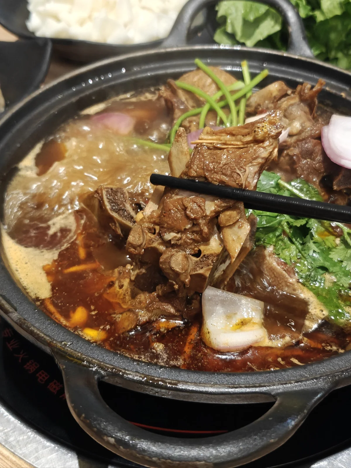 Lamb spine pieces simmering in a bubbling Yang Xiezi hotpot, with chopsticks picking up a marrow-filled bone.