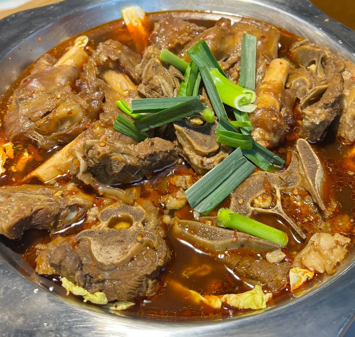 Tender lamb spine chunks cooked in a spicy red broth, topped with scallions in a traditional Yang Xiezi hotpot.