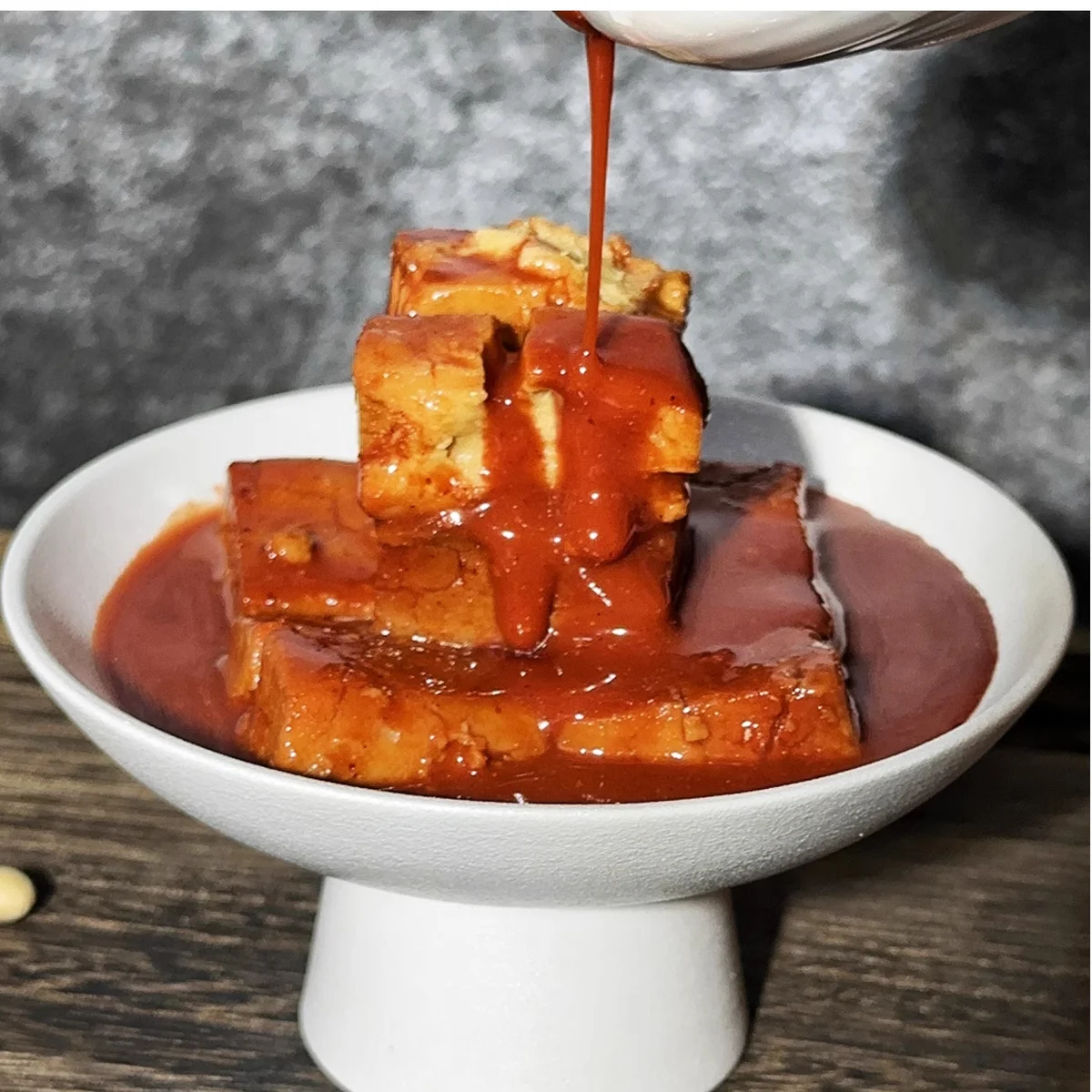 Fermented tofu sauce being poured over tofu cubes, a classic Beijing-style condiment paired with lamb spine hotpot.