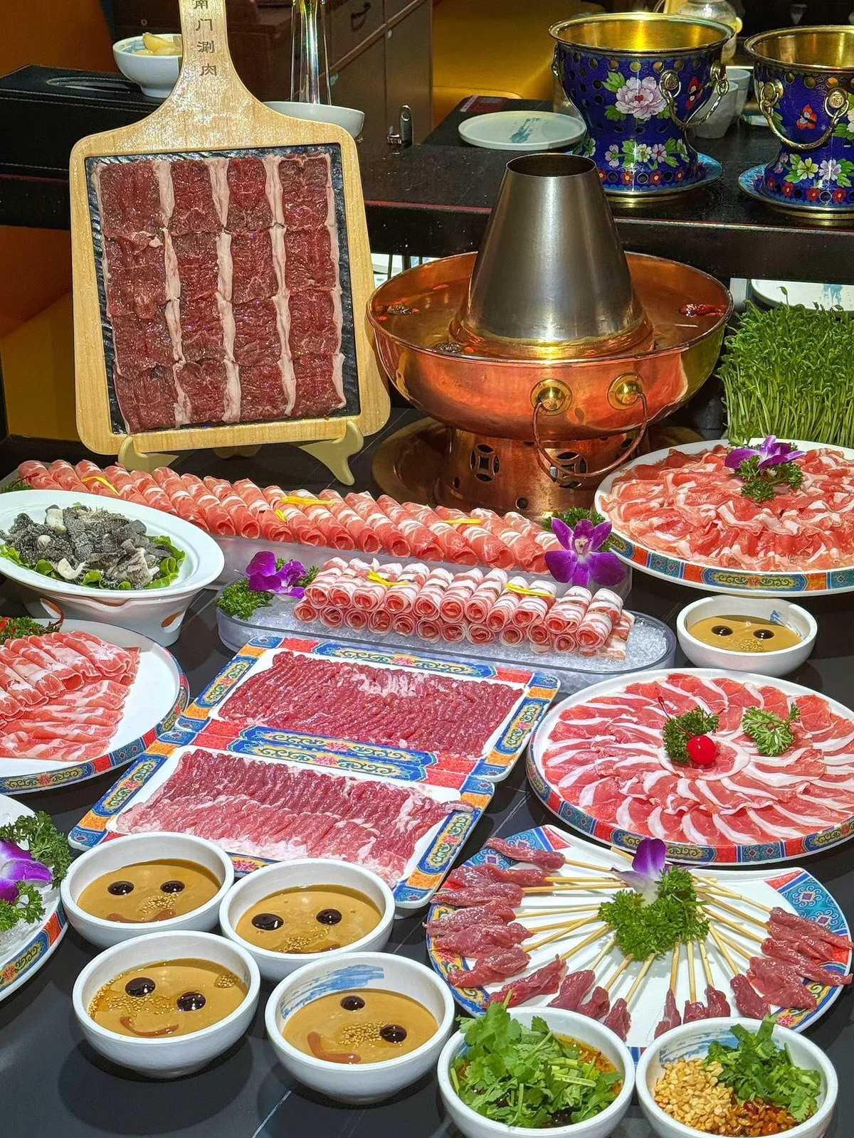 Abundant spread of thinly sliced lamb, vegetables, mushrooms, sesame dipping sauce, and a copper hotpot showcasing a full Beijing Shuan Yangrou feast.