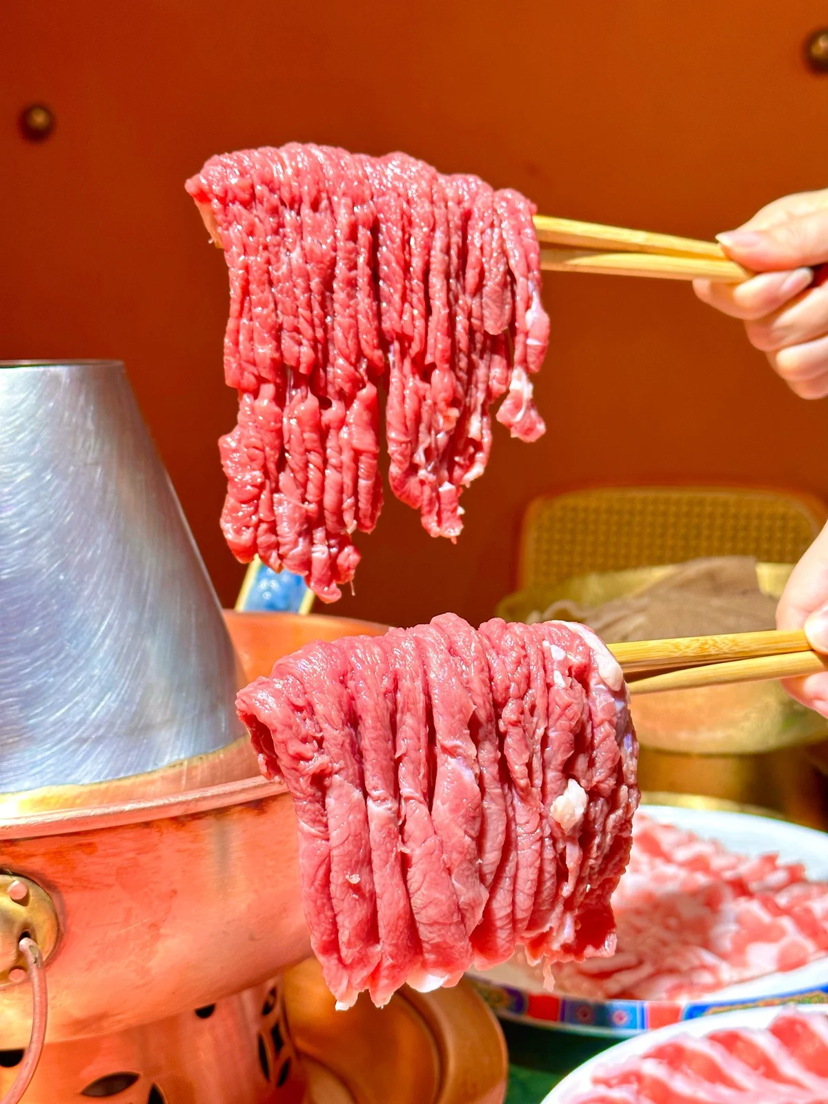 Thick bundles of fresh, thin-sliced lamb held over a steaming copper hotpot, highlighting the signature preparation of Beijing instant-boiled mutton.