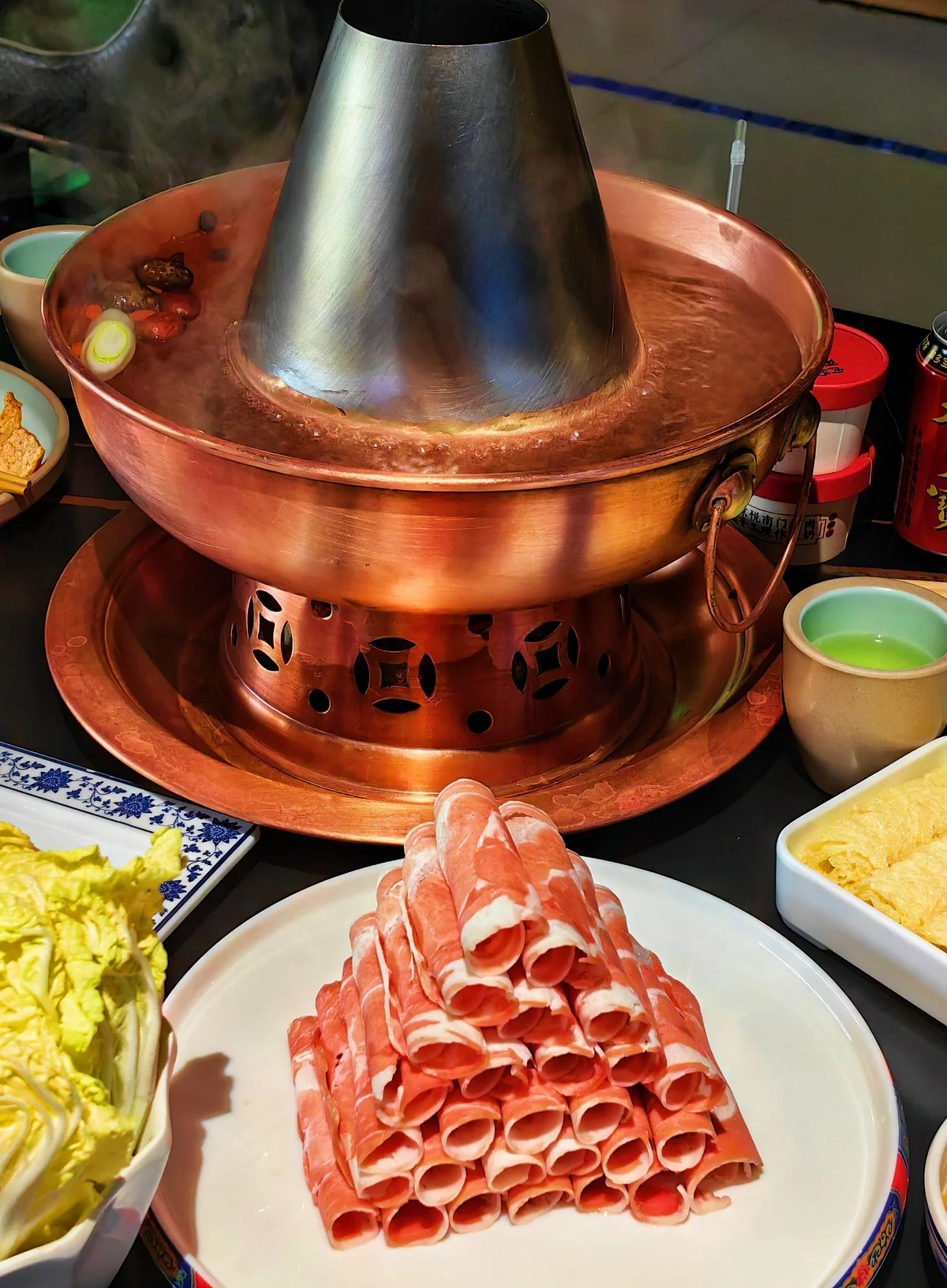 Steaming copper charcoal hotpot with neatly stacked rolls of thin-cut lamb slices prepared for classic Beijing-style instant-boiled mutton.