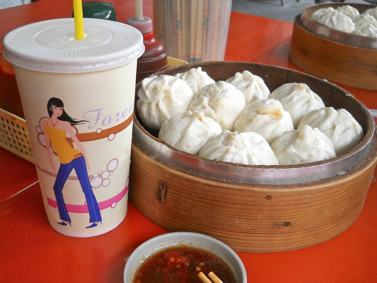 Steamed baozi in bamboo baskets with breakfast drink and chili sauce