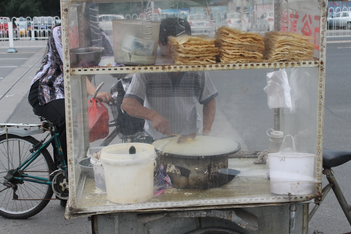 A street vendor preparing jianbing on a round griddle at a breakfast stall.