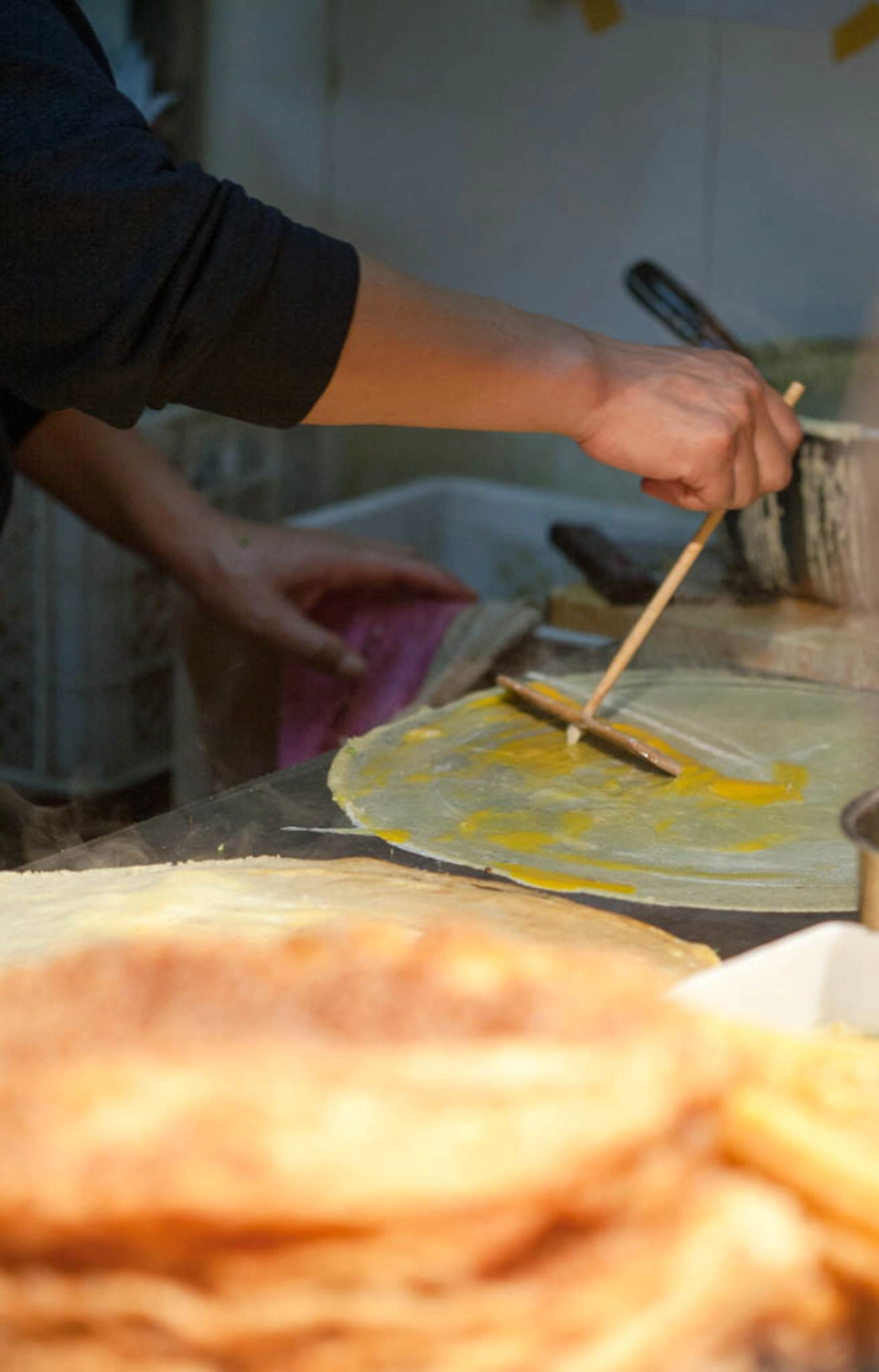 Jianbing being cooked with egg spread across the crepe on a hot griddle.