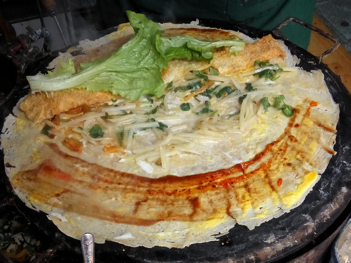 An unwrapped jianbing showing sauce, egg, scallions, lettuce, and the crispy inner layer.