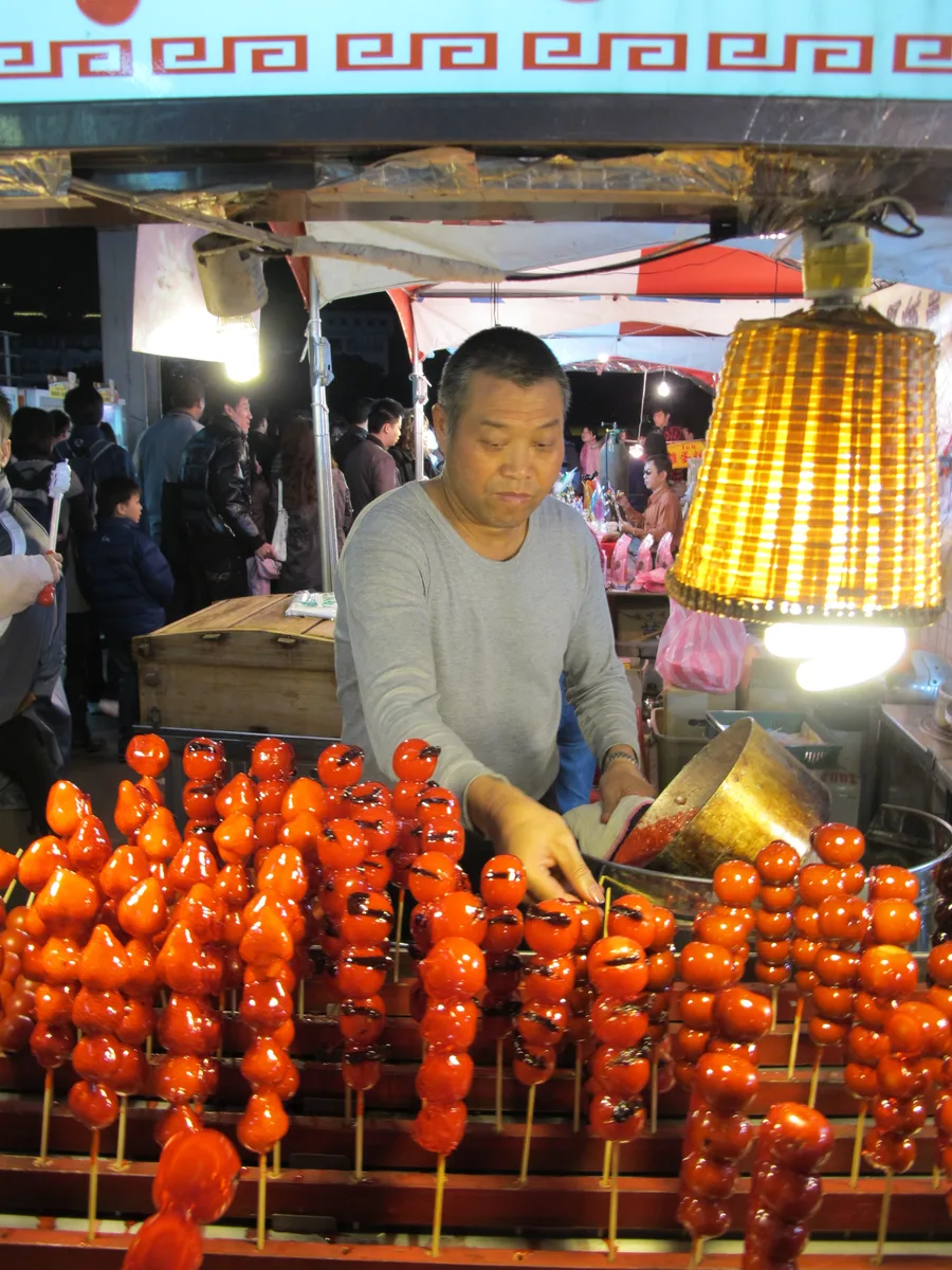 Tanghulu vendor preparing bright red candied hawthorn skewers