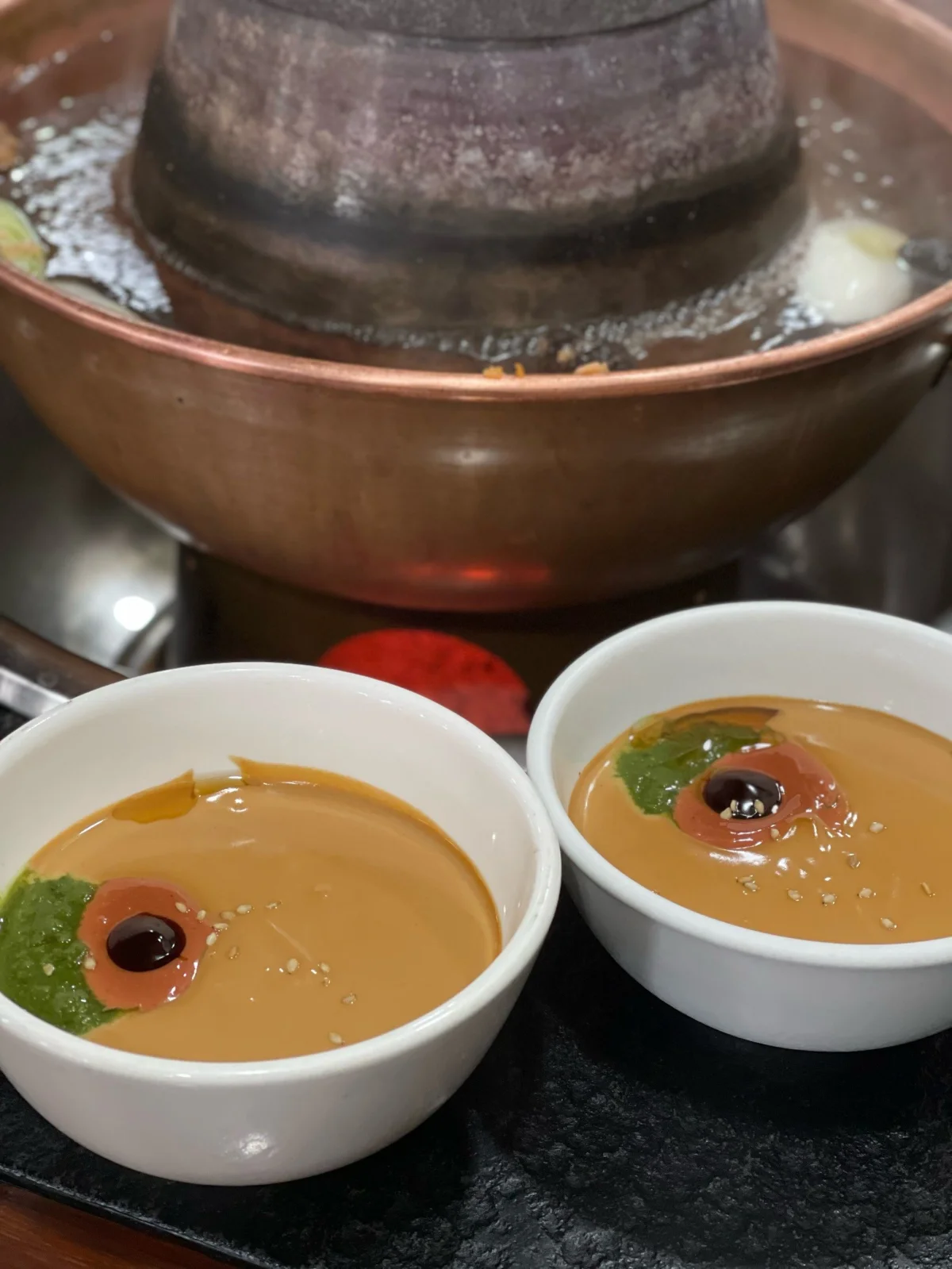 Close-up of sesame paste dipping sauce beside a copper hotpot