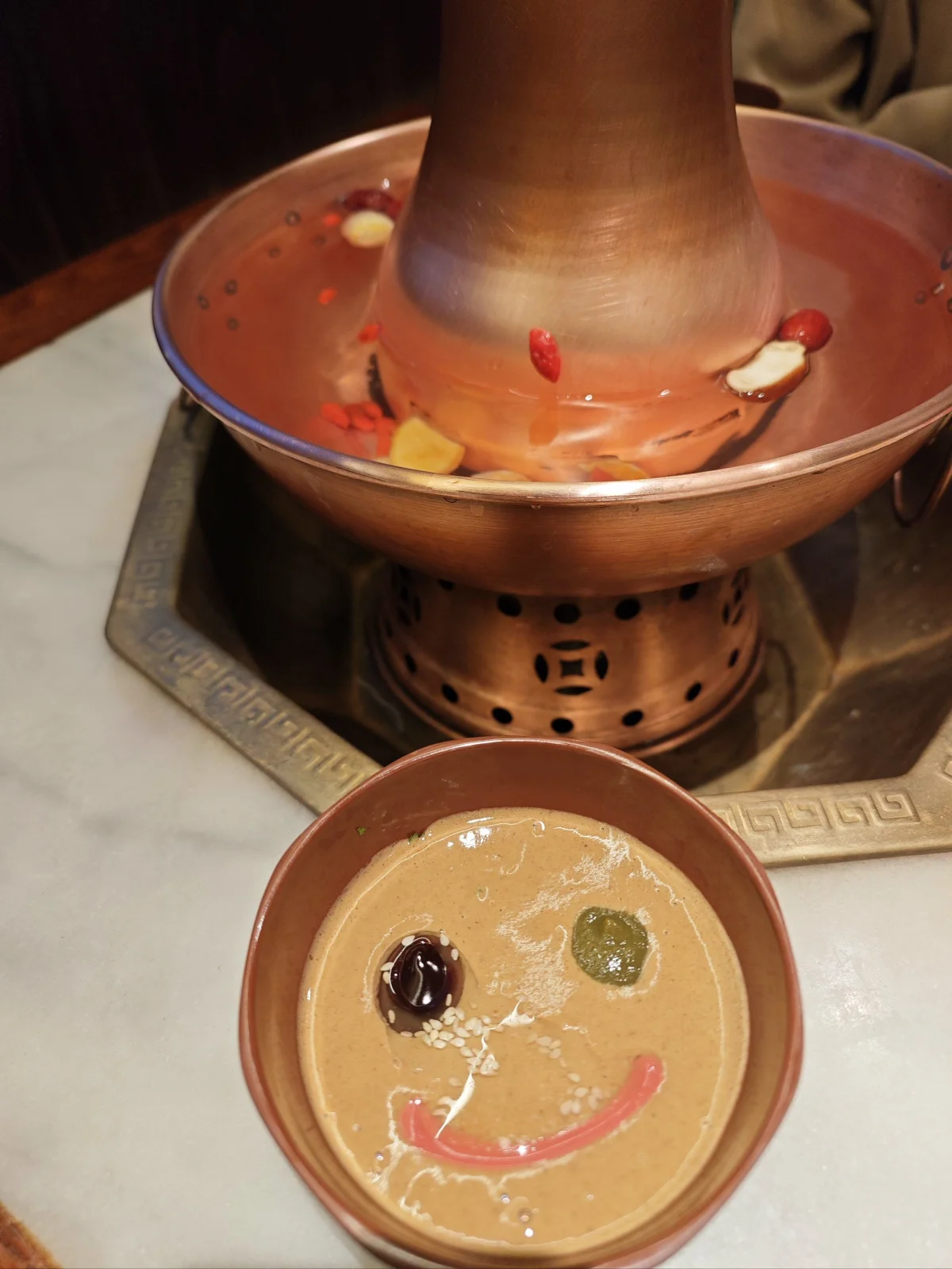 Sesame paste dipping sauce with condiments beside a copper hotpot