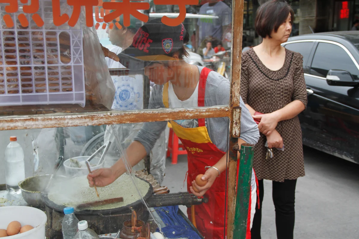 Street vendor preparing a jianbing-style breakfast crepe at a morning stall
