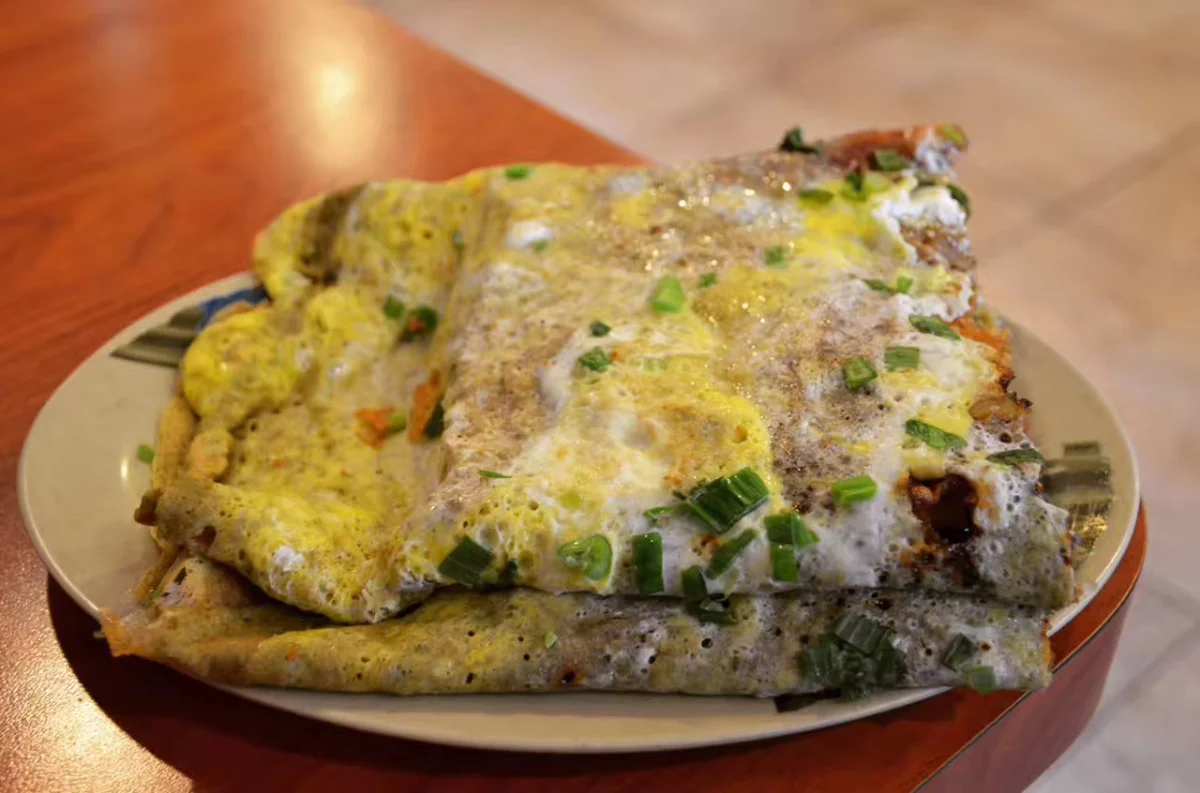 Folded jianbing showing egg, sauce, herbs, and crispy filling on a plate