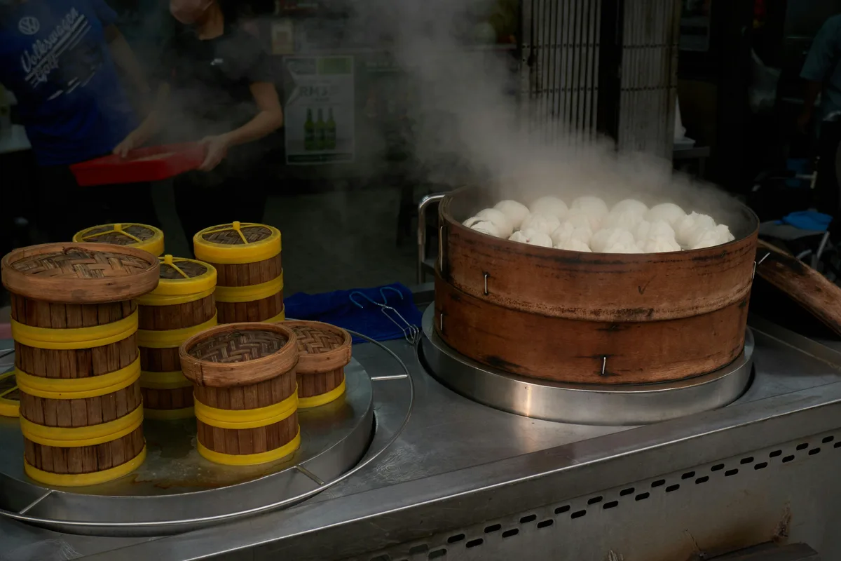 Fresh baozi steaming in a large bamboo steamer at a street food stall