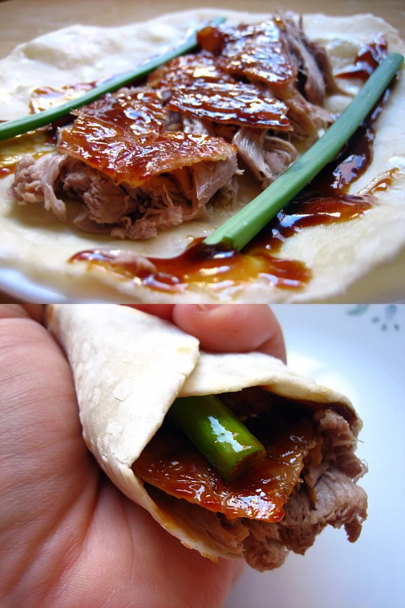 Finished Peking duck pancake wrap held by hand with cucumber and sauce visible