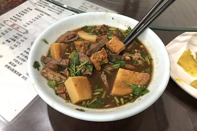Close-up bowl of luzhu huoshao with chopped bread, pork offal, tofu, broth, cilantro, and chopsticks