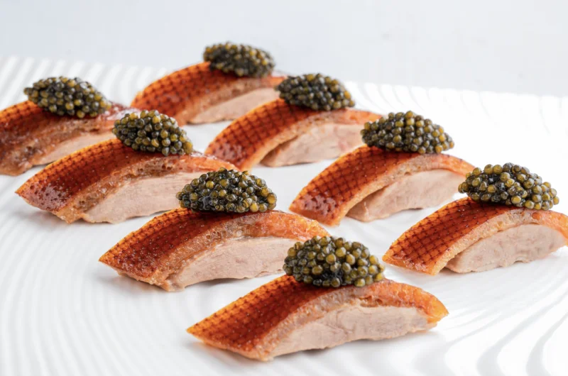 Modern Peking duck skin slices topped with caviar on a white plate