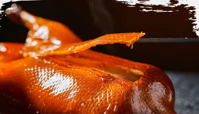 Close-up of glossy Peking duck skin being sliced from a roasted duck