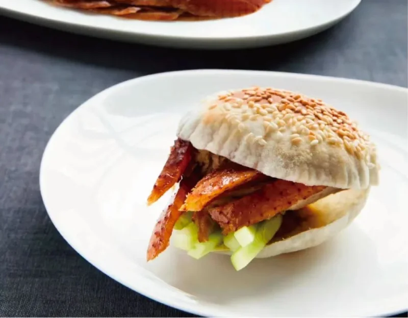 Modern Peking duck bun with roasted duck skin and cucumber on a white plate