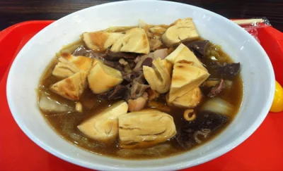 A bowl of Beijing luzhu huoshao with tofu, pork offal, broth, and chopped huoshao bread
