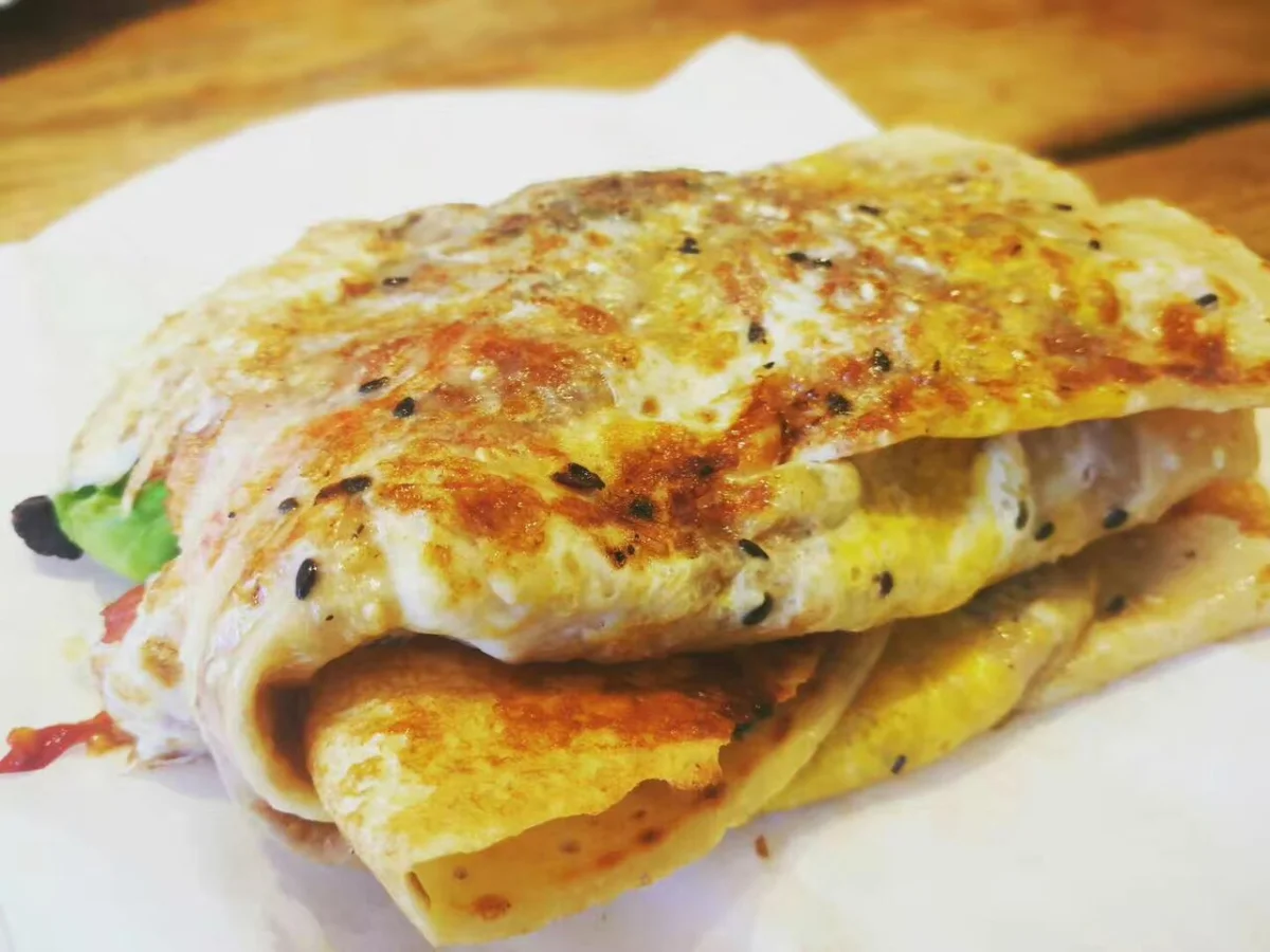 Folded jianbing guozi showing egg, sauce, herbs, and a crisp cracker layer inside the crepe