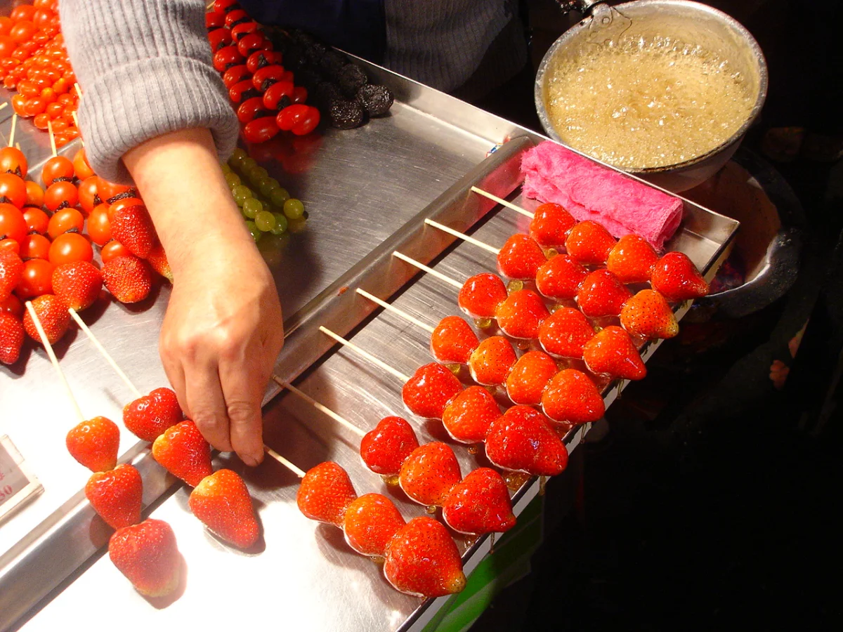 Vendor coating fresh fruit skewers with hot sugar for tanghulu
