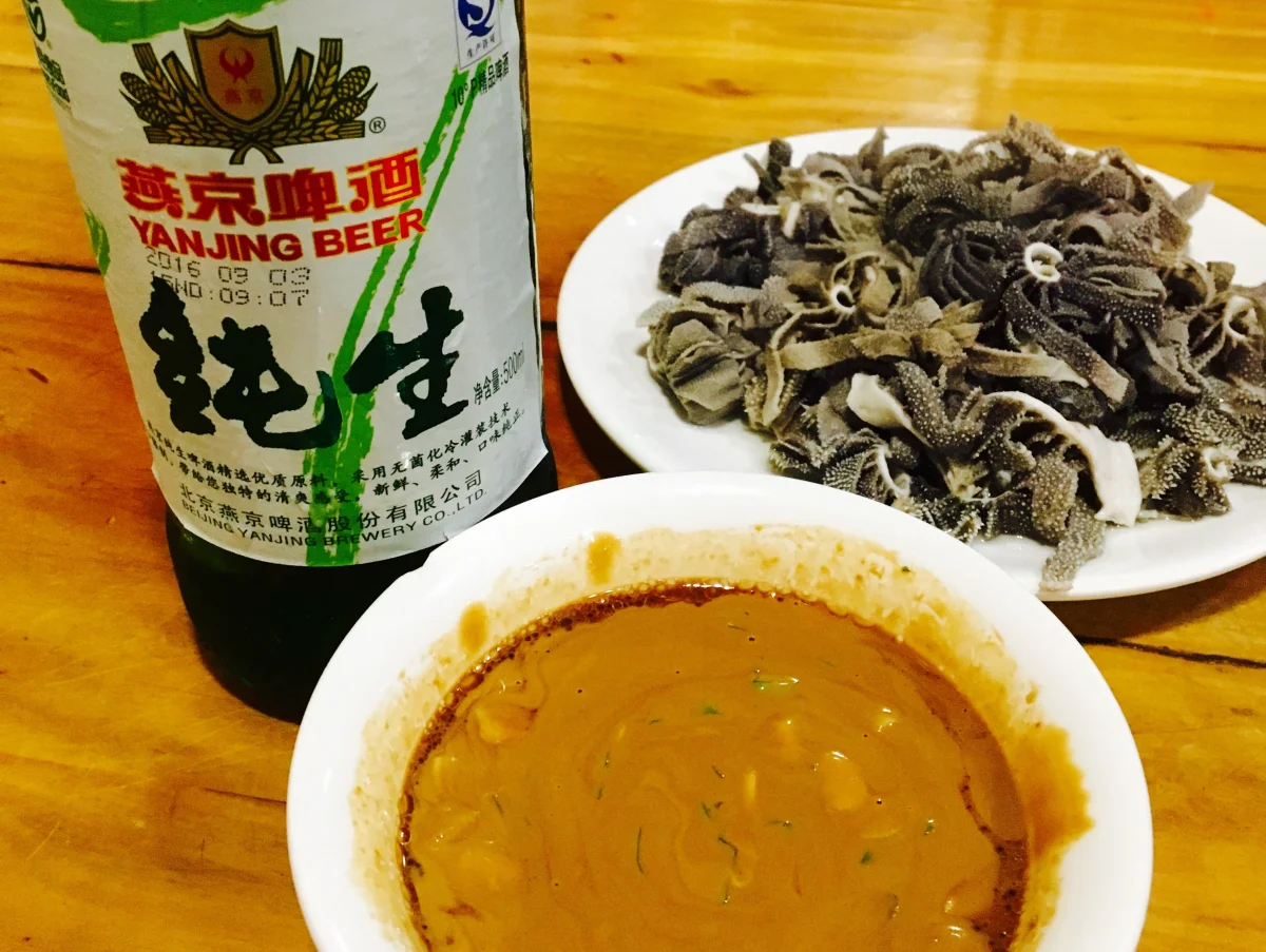 Lamb tripe baodu with rich sesame dipping sauce and beer on the table