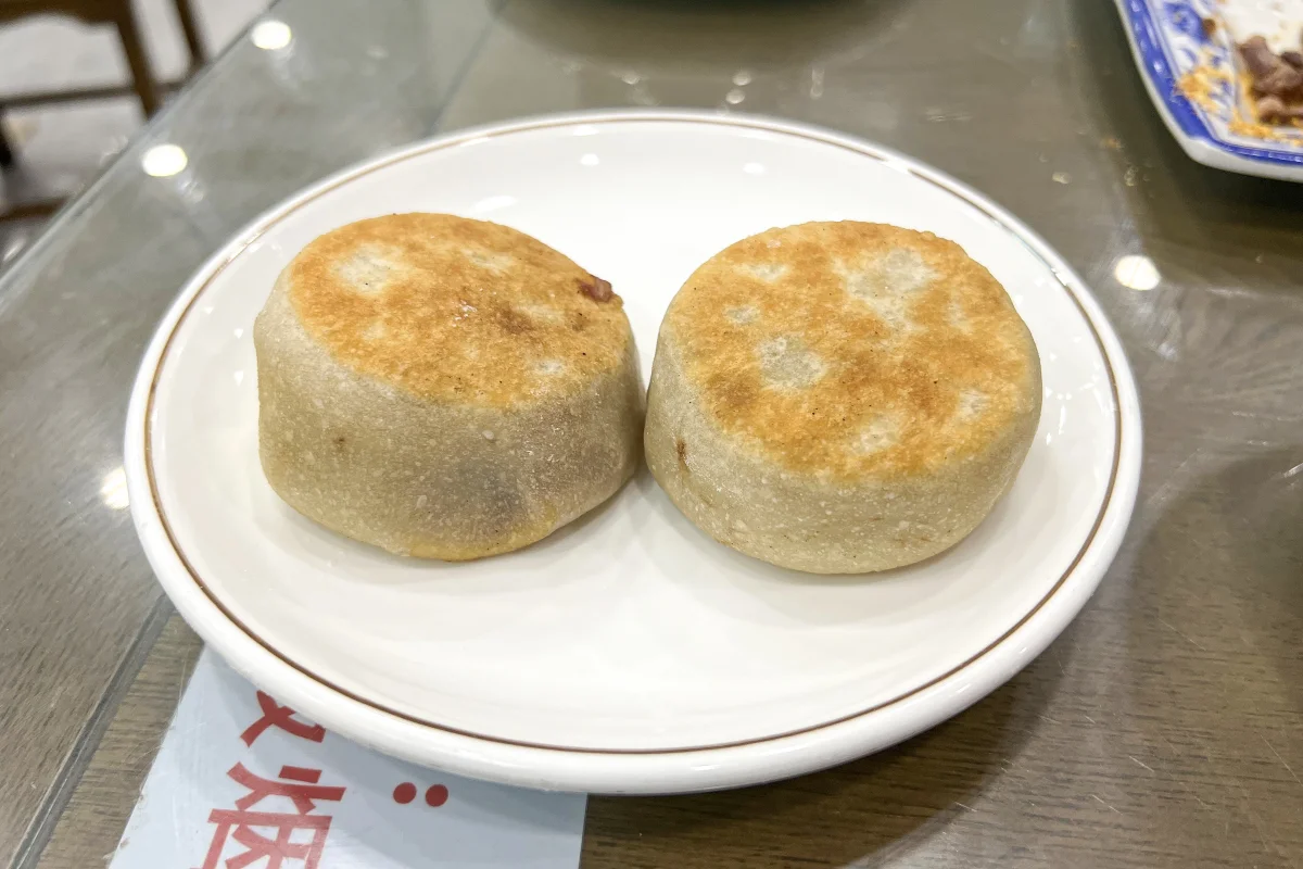 Two men ding rou bing meat pies served on a small plate in a Beijing snack shop
