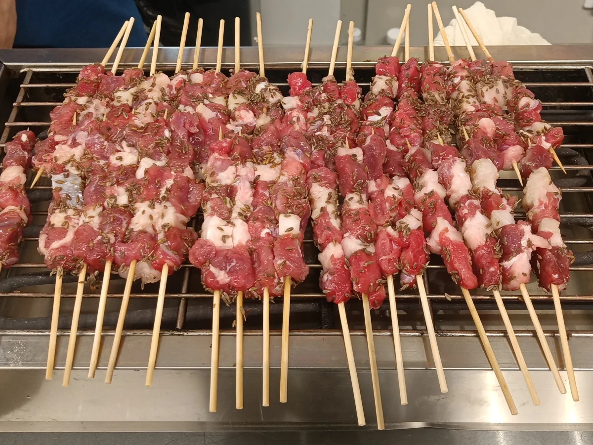 Fresh lamb skewers arranged over a grill before cooking