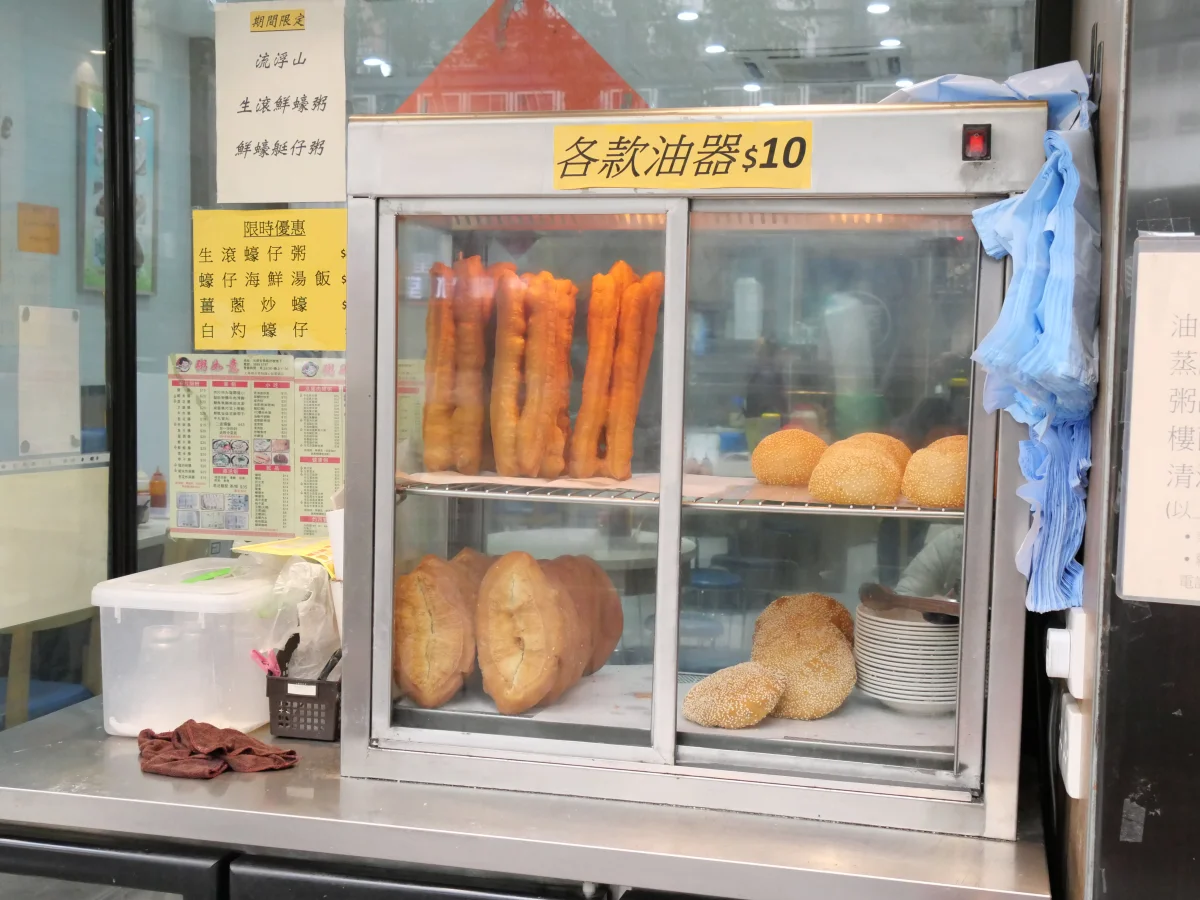 A breakfast counter display with youtiao among other fried dough foods at a congee shop.