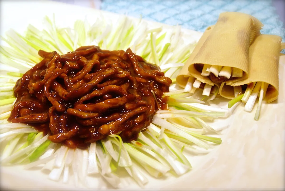 Sweet bean sauce-coated pork with a large bed of scallion and folded tofu skin wrappers.