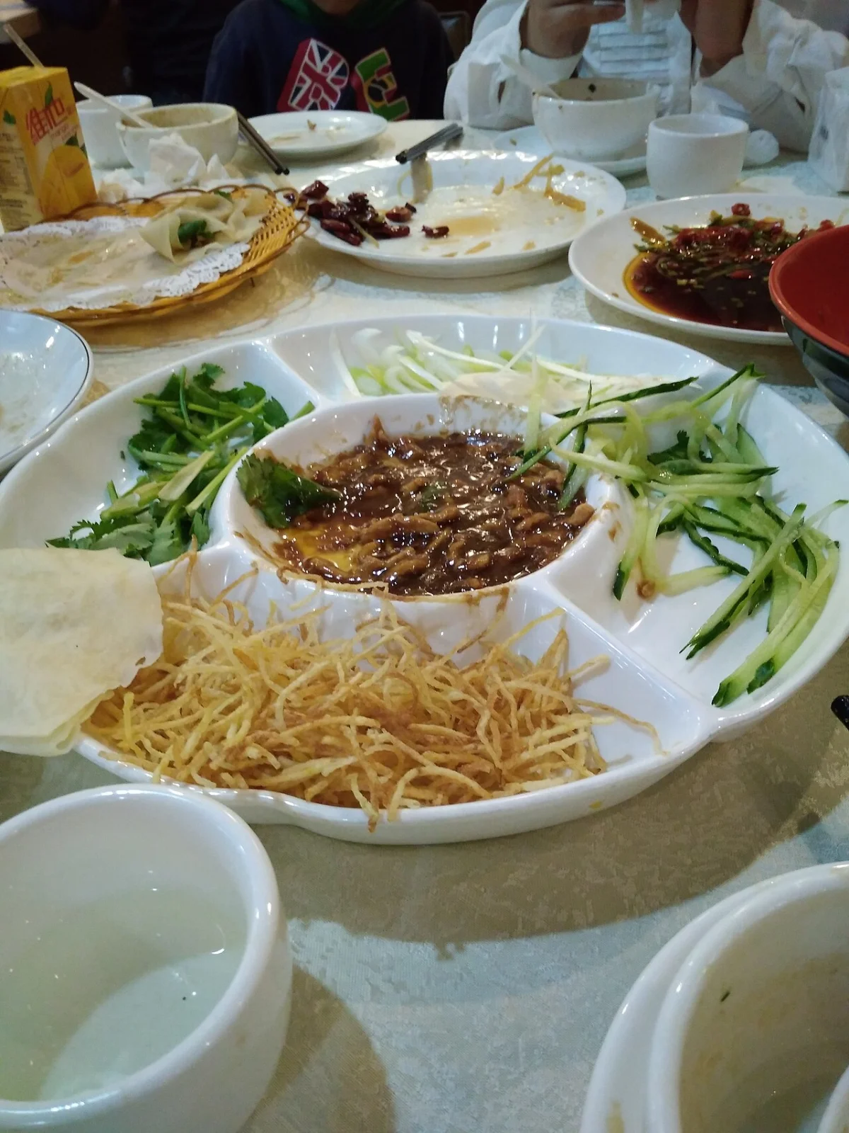 A table setting showing Jing Jiang Rou Si with tofu skin, scallion, and thin pancakes.