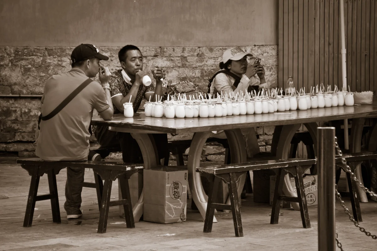 People drinking yogurt beside a row of traditional ceramic yogurt jars in Beijing.