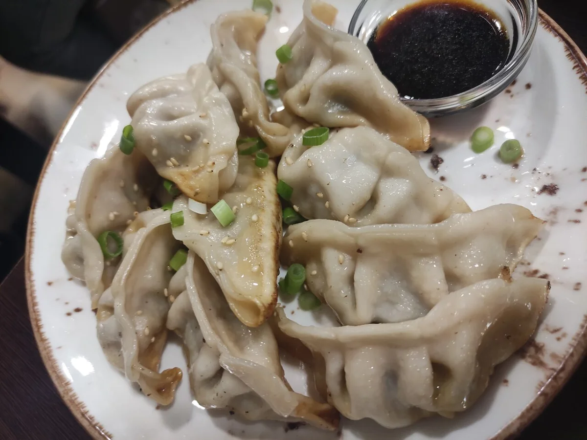 Pan-fried dumplings with a separate dark dipping sauce, photographed in Spain