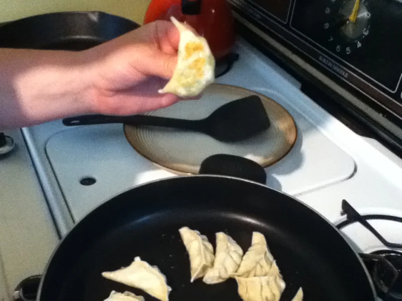 A home cook checking the browned base of a potsticker beside the frying pan