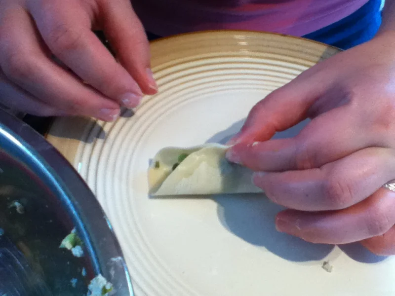 Hands folding a dumpling wrapper around a vegetable filling during home potsticker preparation